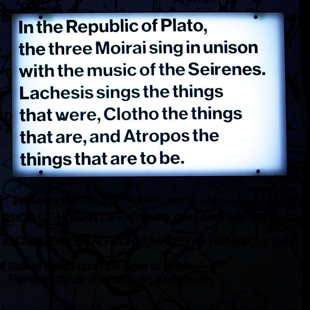 Illuminated text panel describes the three Moirai singing what was, what is, and what is to be.
