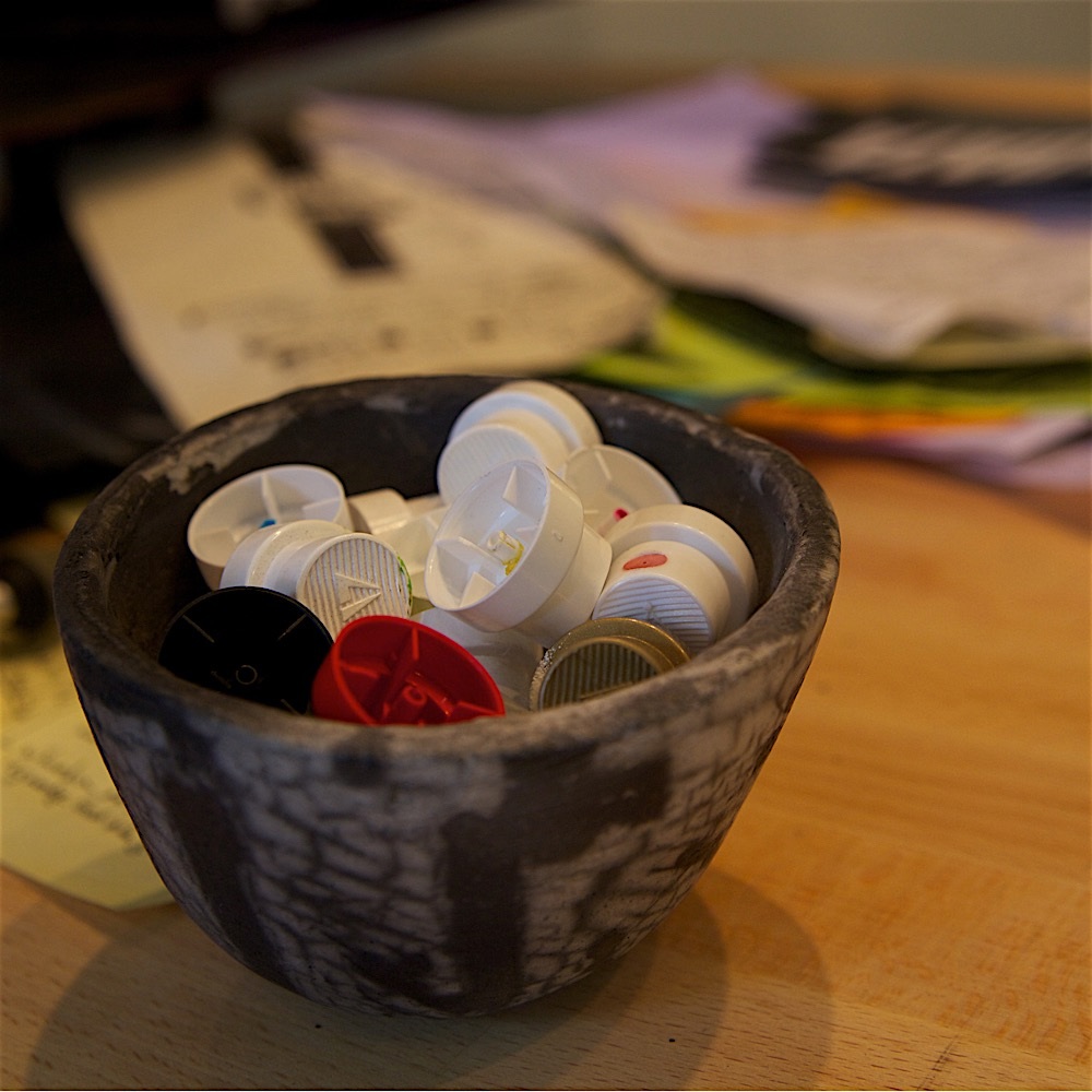 Small colored components sit in a dark bowl on a worktable scattered with paper notes.